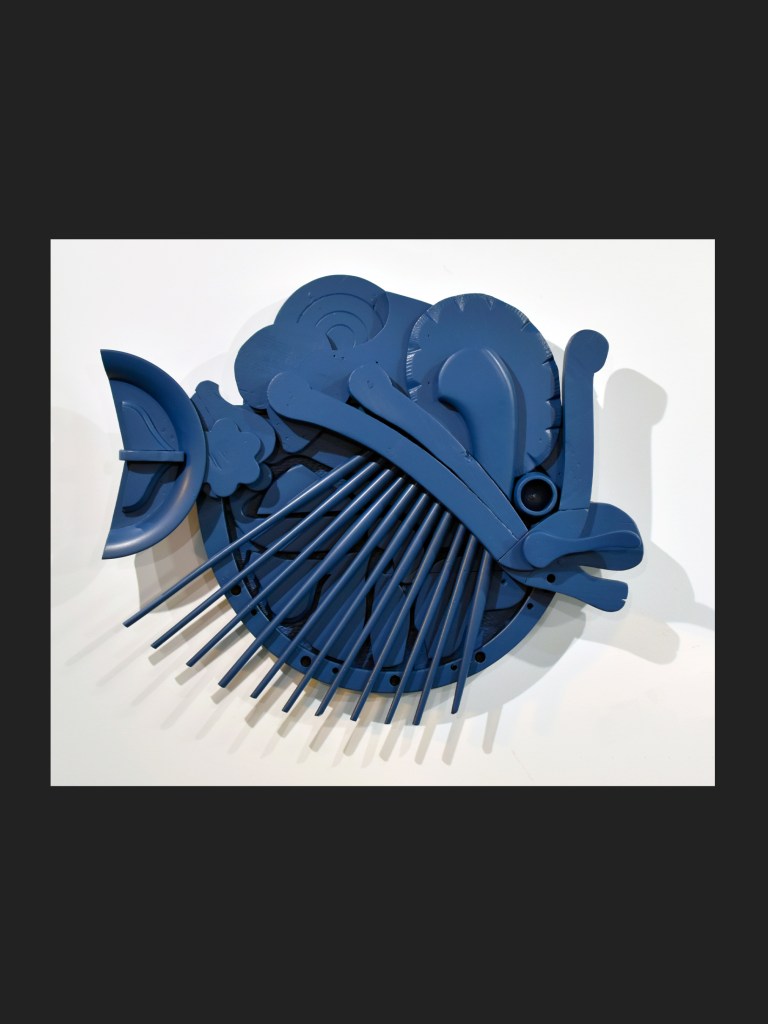 An abstract wall installation of a fish made from reclaimed wood featuring a variety of blue shapes and forms and playful designs by David Furman