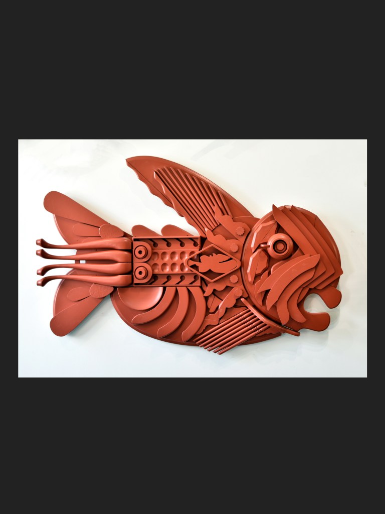 A decorative wall sculpture of a fish, made from reclaimed wood featuring a textured and layered design in a reddish-brown color by David Furman