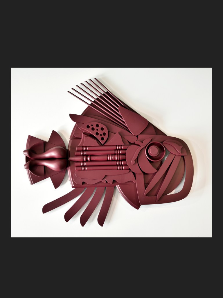 A decorative artwork resembling a fish, created from reclaimed wood using various shades of burgundy colors and abstract shapes by David Furman