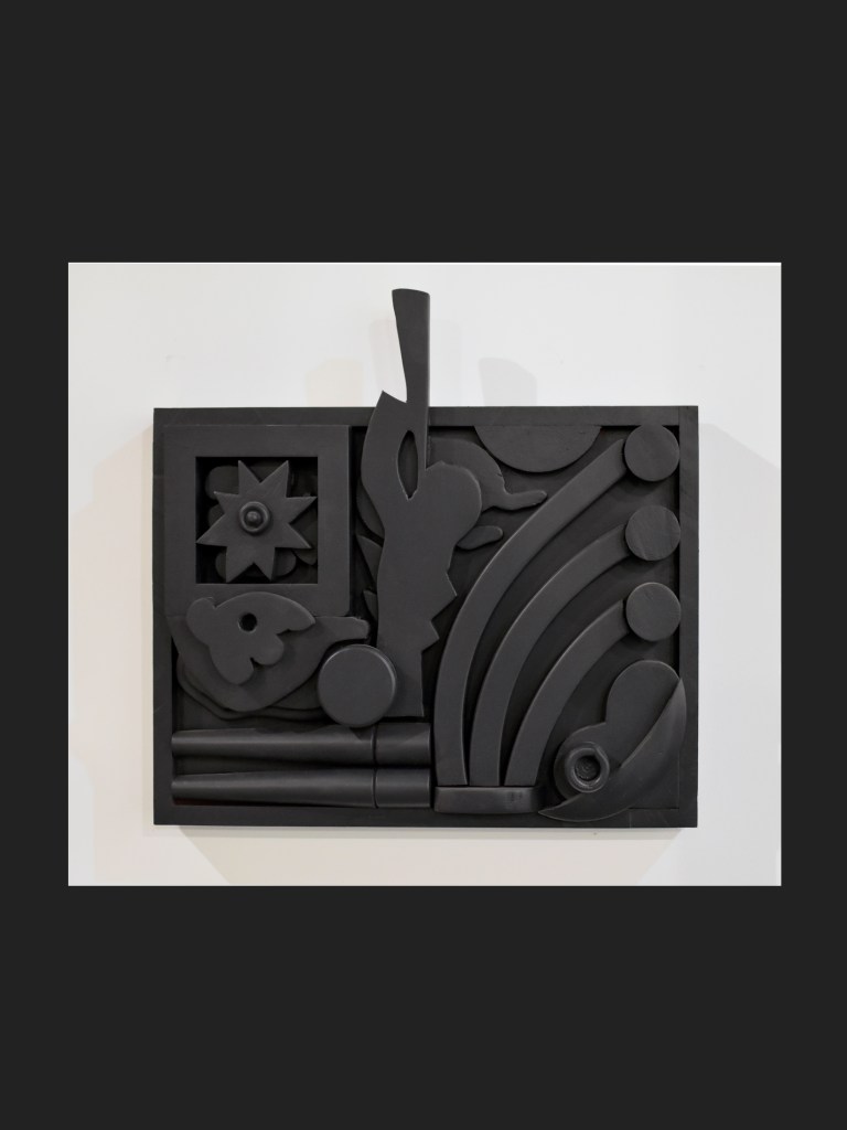 A hanging wall sculpture artwork made from reclaimed wood featuring various geometric and organic shapes including circles, curves, and abstract forms on a white background by David Furman