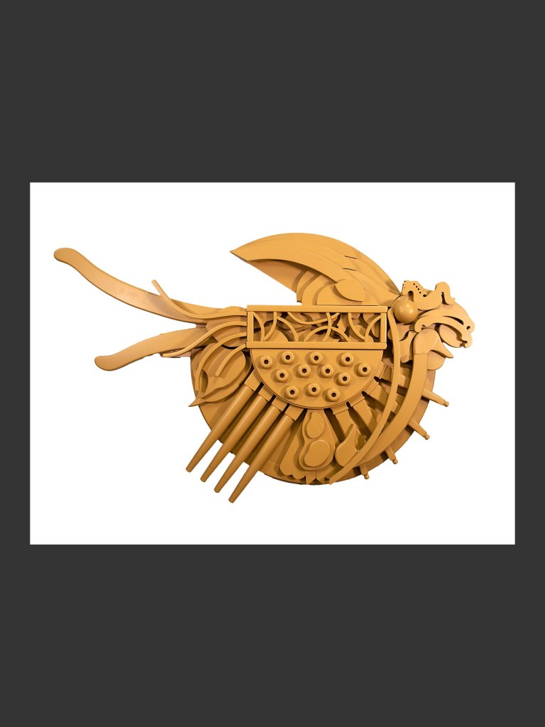 A wall sculpture of a fish made in an intricately geometric form made from reclaimed wood and painted yellow by David Furman