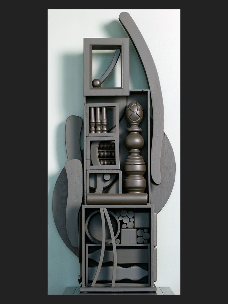 A modern abstract wall sculpture made from reclaimed wooden pieces composed of various geometric shapes and forms, arranged in a vertical composition, predominantly in dark gray tones by David Furman