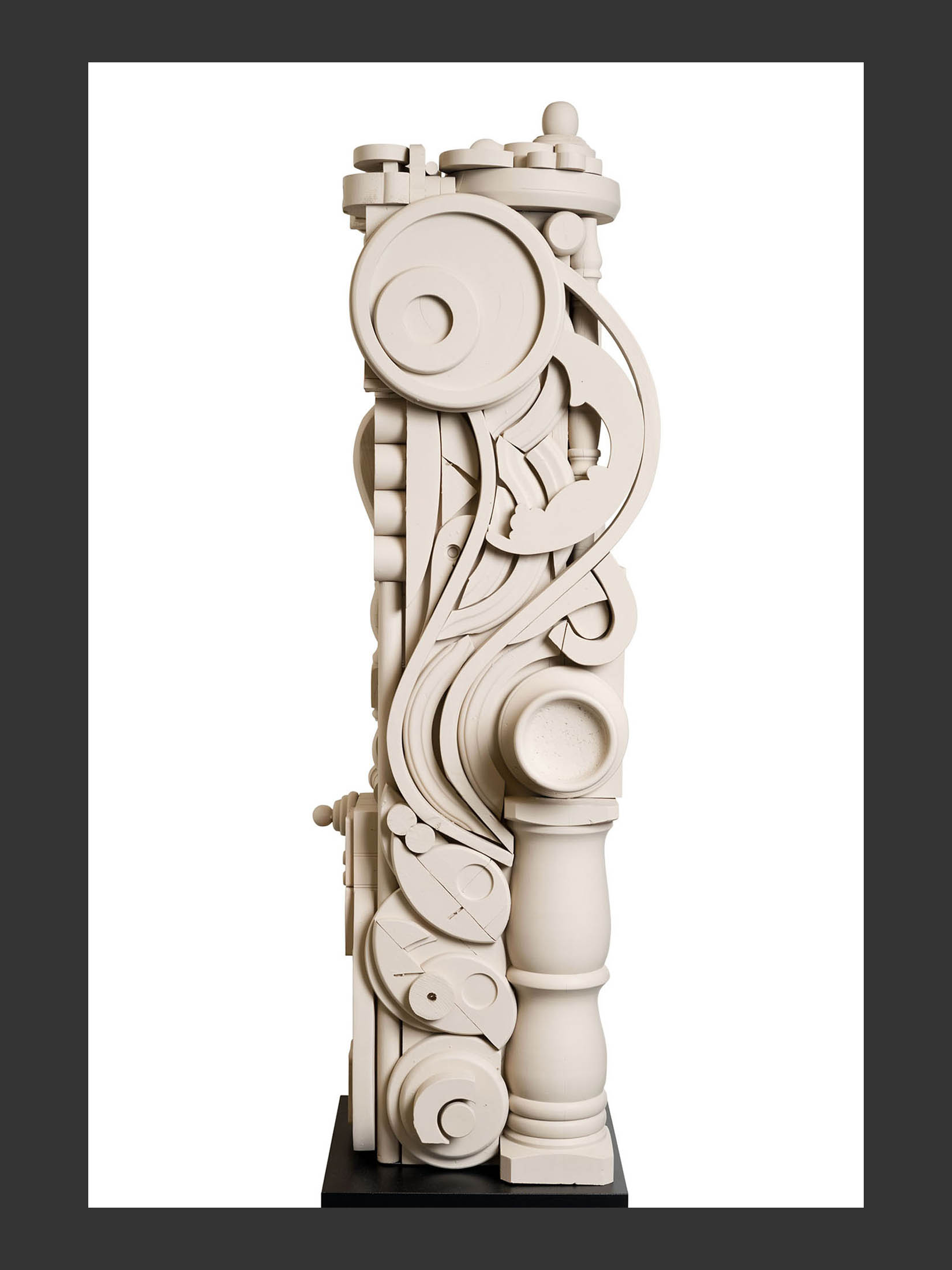 A tall, abstract white totem sculpture made from reclaimed wood elements featuring curved and circular designs with intricate detailing, standing on a black base by David Furman