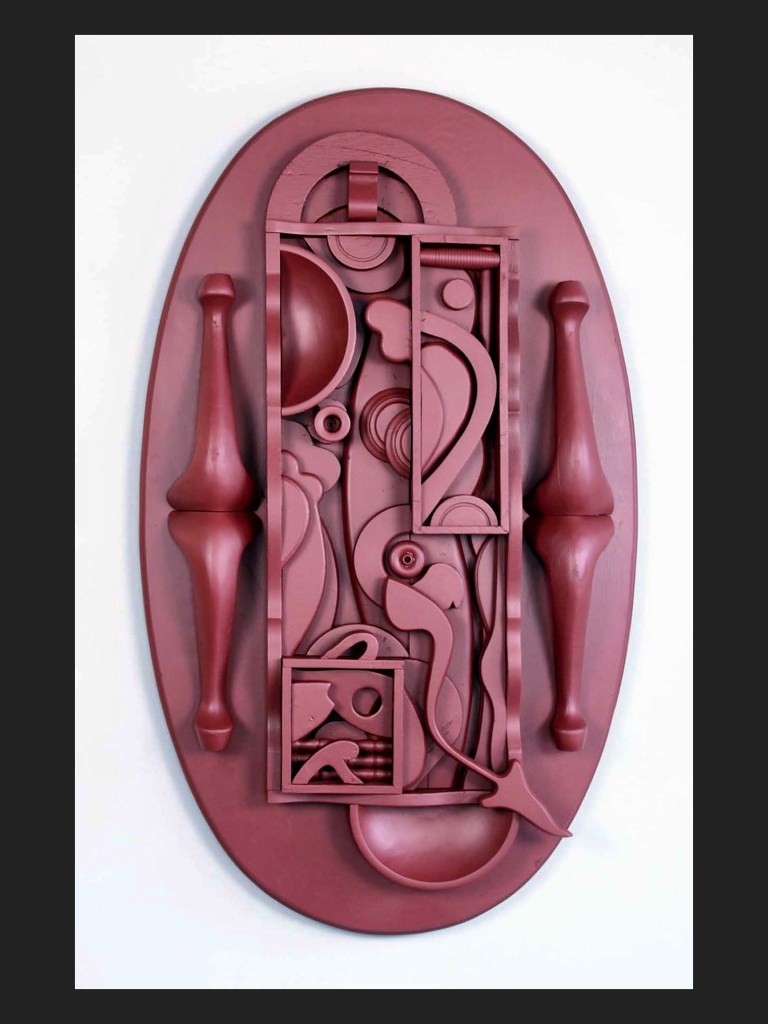 A three-dimensional wall sculpture artwork made from reclaimed wooden elements and featuring abstract shapes and forms in a reddish-brown color, set against a black background by David Furman