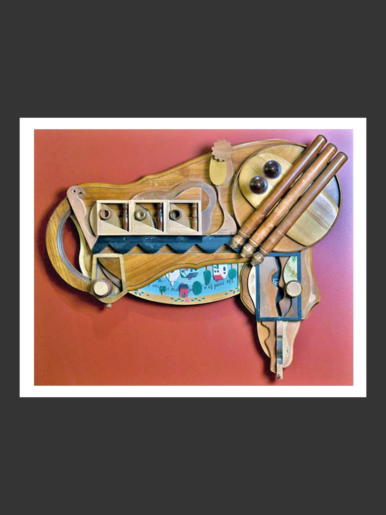 A colorful wooden wall sculpture made from reclaimed wooden elements, featuring various shapes and objects and a decorative base by David Furman