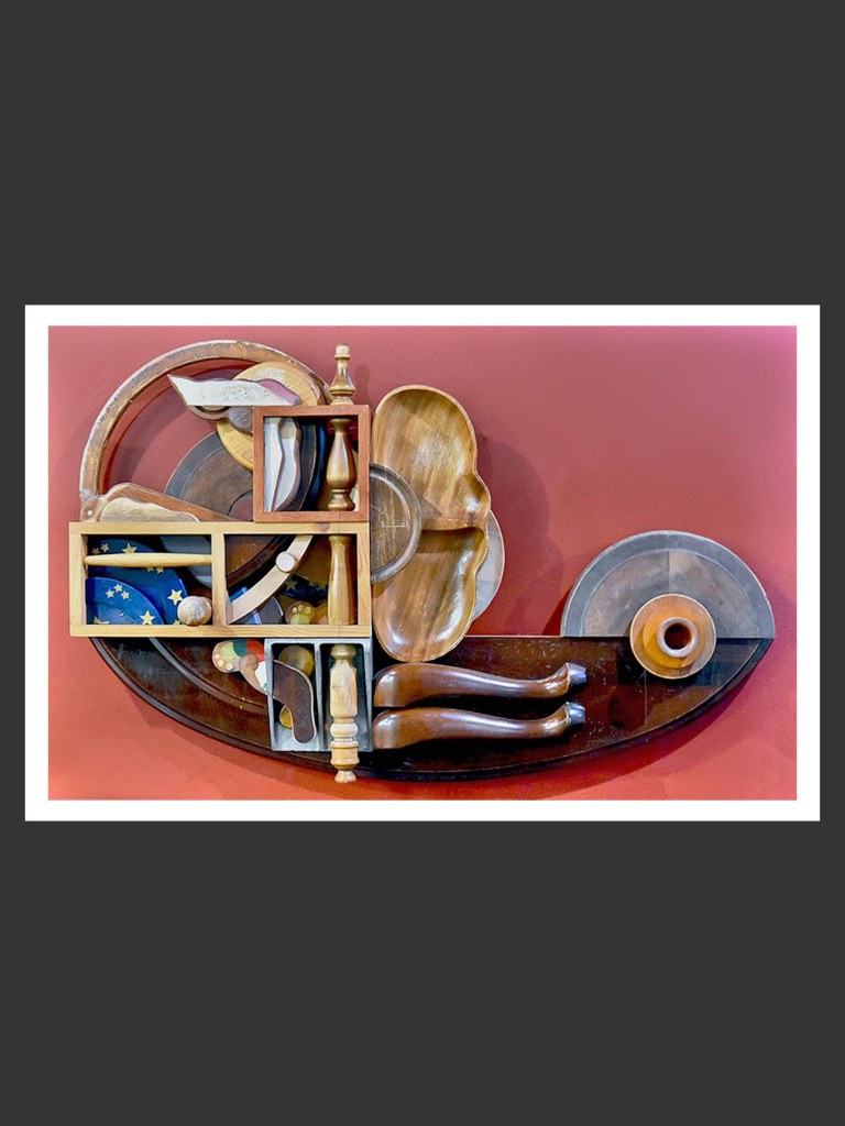 A wall sculpture made from a collection of wooden objects arranged artistically on a red background, showcasing various shapes and sizes of bowls, trays, and other forms artistically formed into a beguiling arrangement by David Furman 