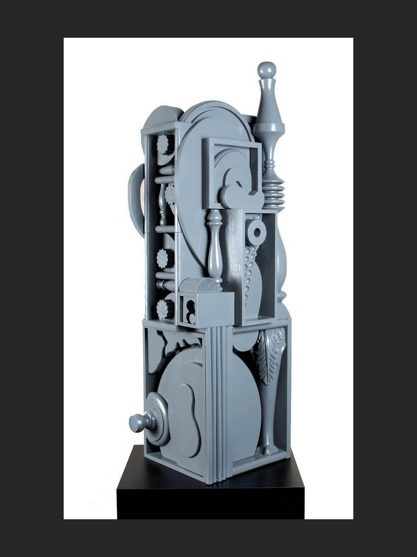 A gray abstract sculpture made from reclaimed wood featuring geometric shapes and mechanical elements, displayed on a pedestal by David Furman.