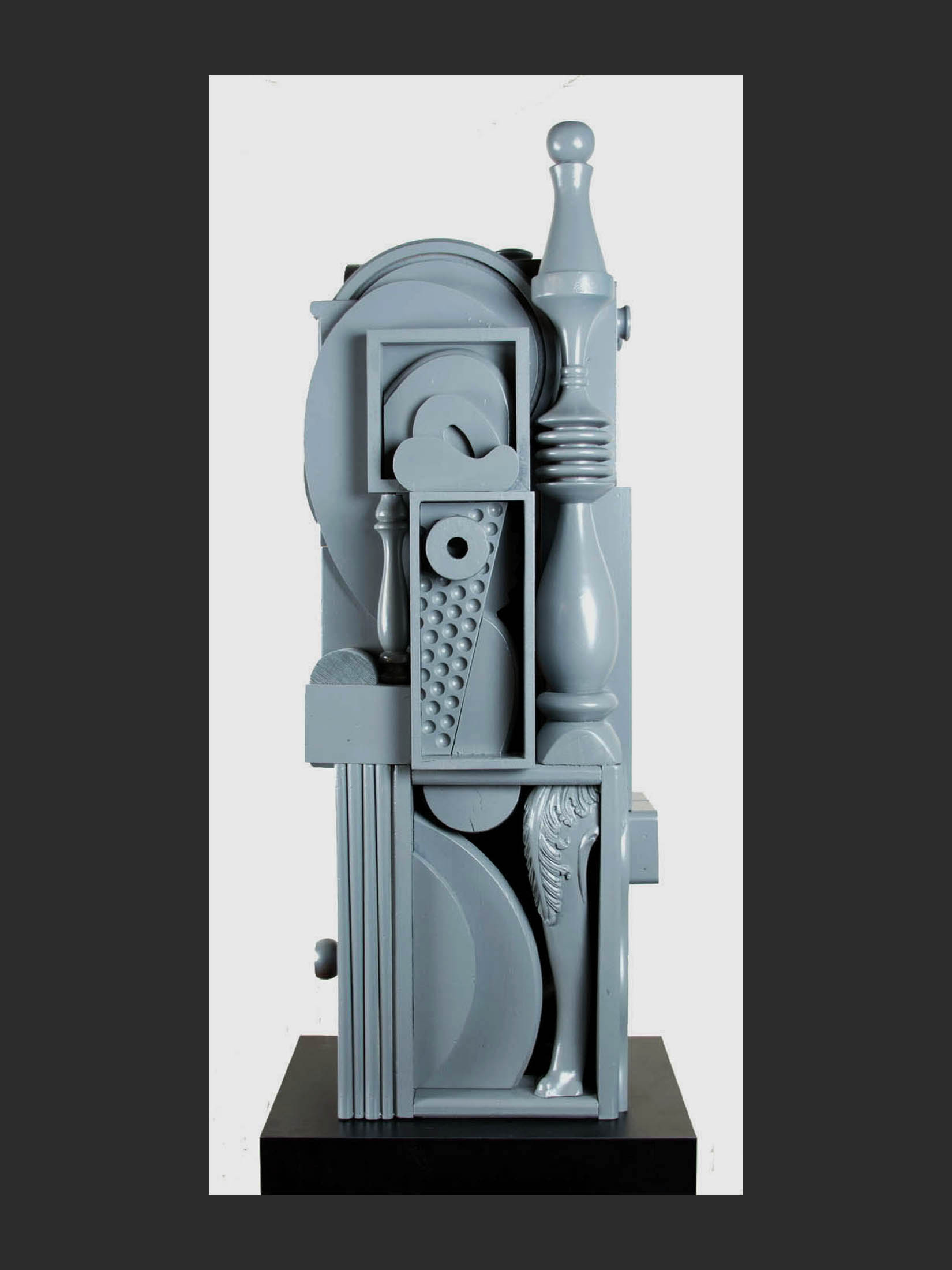 An abstract gray pedestal sculpture constructed from reclaimed wood and composed of geometric shapes, curves, and textured elements, arranged vertically by David Furman