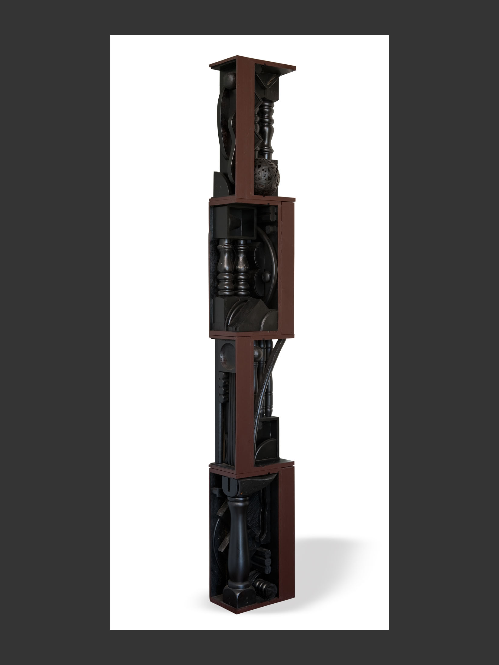 A tall, stacked sculpture, or “Totem”, made of repurposed wood featuring various geometric forms and dark-colored elements by David Furman.